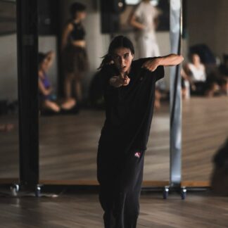The picture shows teacher Montse dancing in the studio, looking at the camera and extending their arms