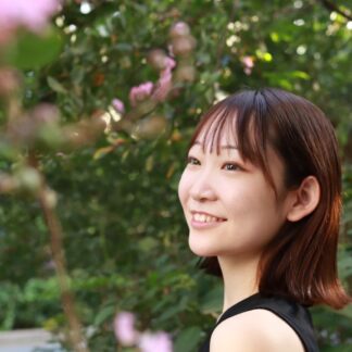 This picture shows teacher Sakika outside in a garden, smiling, looking away from the camera
