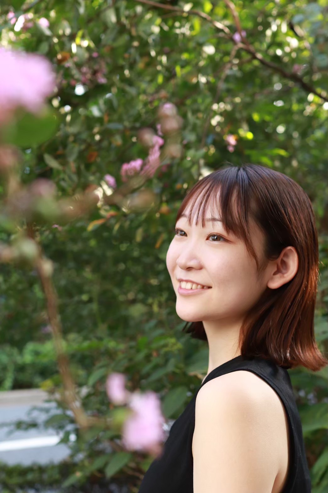 This picture shows teacher Sakika outside in a garden, smiling, looking away from the camera